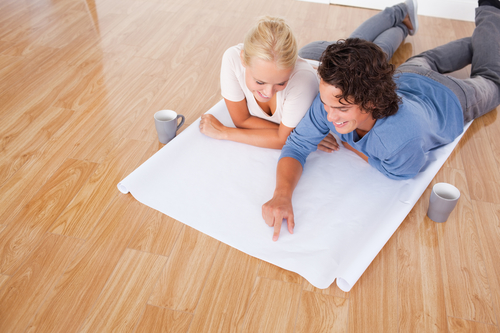 Young man showing a point on a plan to his fiance while lying on the floor